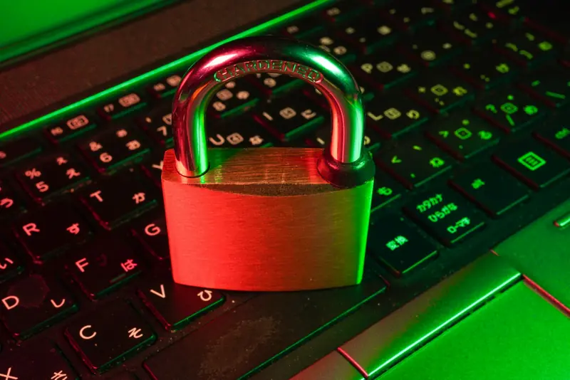 A brass padlock resting on a laptop keyboard lit in red and green