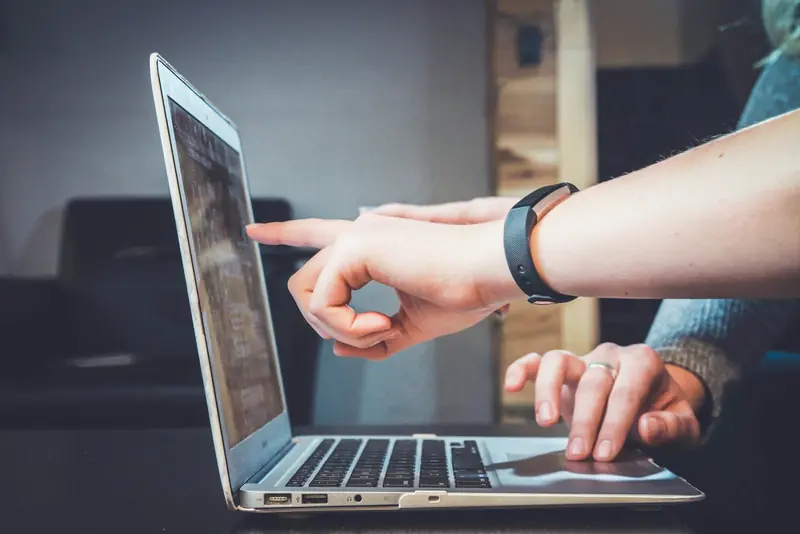 Two people at a laptop, one pointing at something on the screen