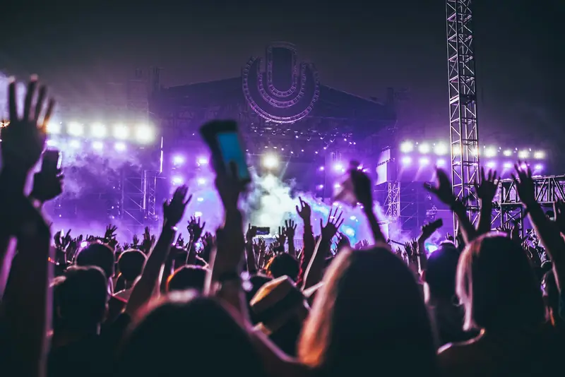A concert crowd with raised hands under purple stage lights