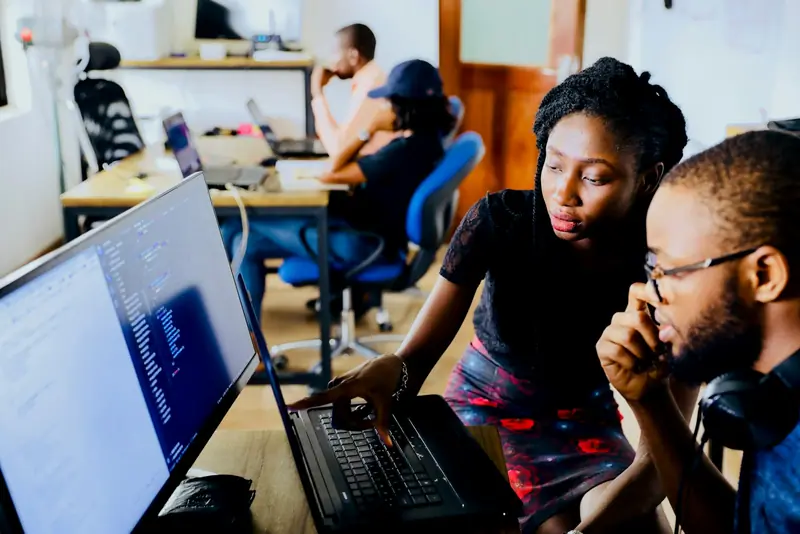 Two colleagues reviewing code together on a laptop
