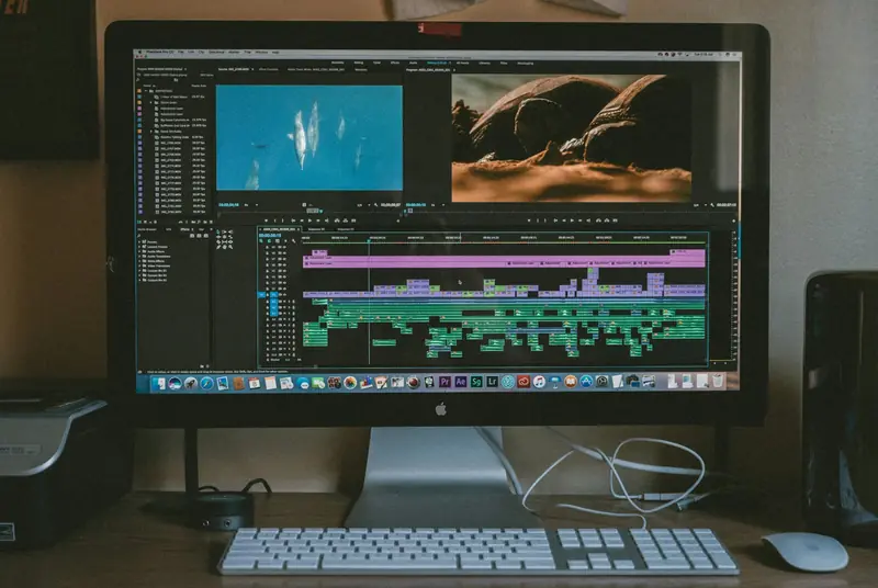 An iMac showing a video-editing timeline and two preview clips