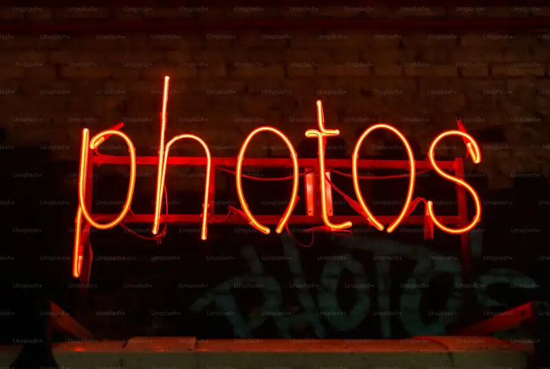 A red neon sign spelling “photos” on a brick wall
