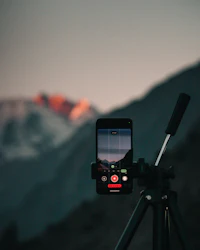 A smartphone on a tripod recording video of mountains at dusk